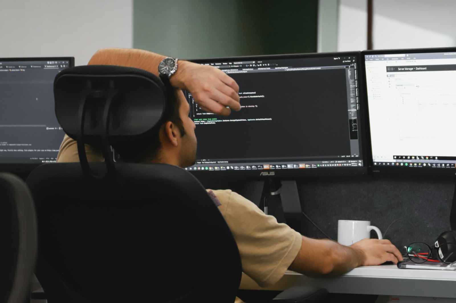 A developer working at a three-monitor workstation, seen from behind